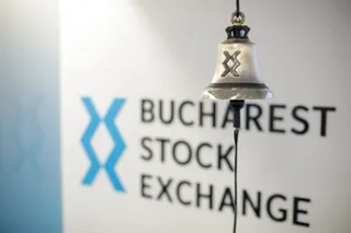 Un clopot metalic cu un simbol gravat este suspendat în fața unui perete alb pe care scrie Bucharest Stock Exchange.
