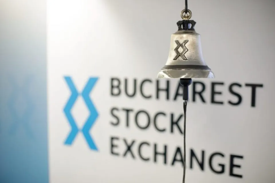 Un clopot metalic cu un simbol gravat este suspendat în fața unui perete alb pe care scrie Bucharest Stock Exchange.