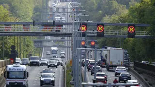 Mașini și camioane circulă pe o autostradă cu panouri de semnalizare deasupra benzilor de rulare.