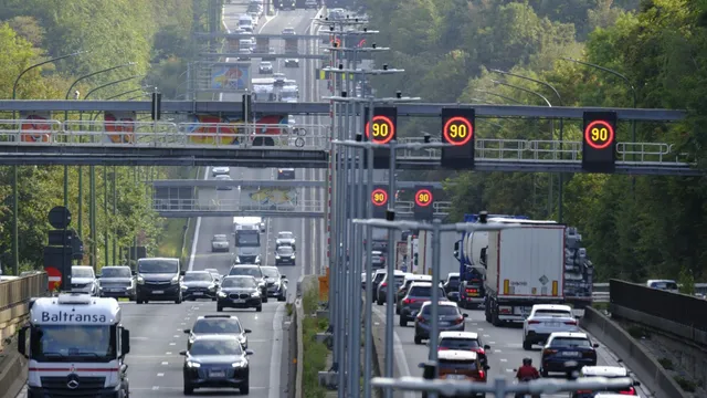 Mașini și camioane circulă pe o autostradă cu panouri de semnalizare deasupra benzilor de rulare.