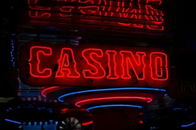 Un semn de neon roșu luminează cuvântul CASINO pe un fundal întunecat, înconjurat de alte linii de lumină albastră și roșie.