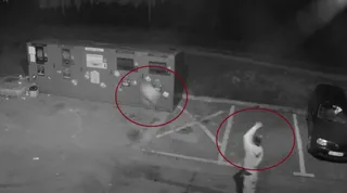 O imagine alb-negru de supraveghere surprinde două zone cerculate în roșu pe un teren asfaltat lângă un container mare și o mașină în parcarea de lângă acesta.