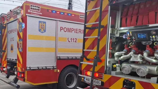 Un camion de pompieri roșu cu compartimente deschise și o scară este parcat pe o stradă.