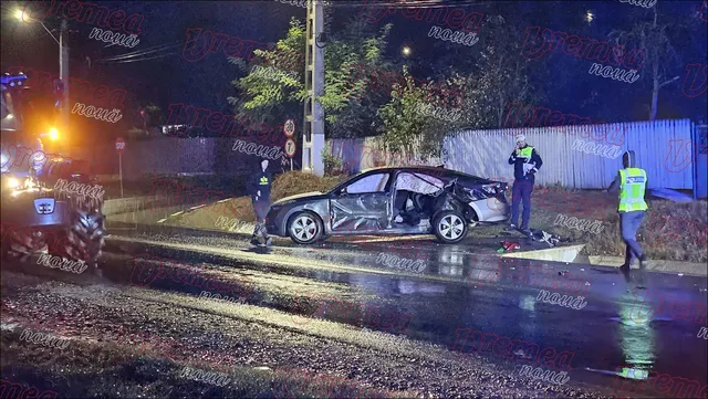 Un autoturism negru este oprit pe un drum umed lângă un vehicul de serviciu, în prezența unor persoane purtând veste reflectorizante.