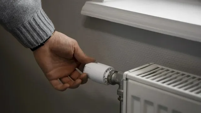 O mână întinde degetele spre un robinet alb de pe un calorifer metalic situat sub un pervaz alb.