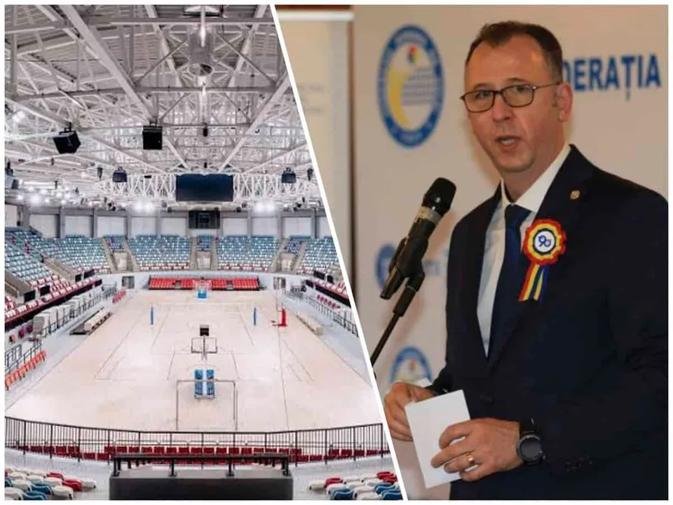 Un bărbat cu ochelari și un rozetă colorată stă în fața unui microfon, lângă o imagine cu interiorul unei săli de sport cu tribune și teren.
