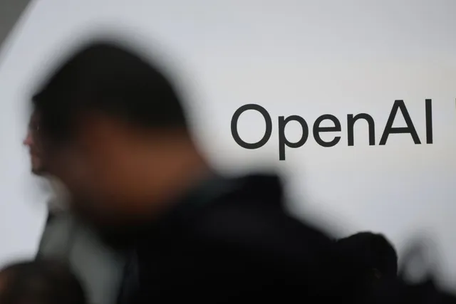 Un logo cu textul OpenAI este afișat pe un fundal alb lângă silueta neclară a unei persoane.