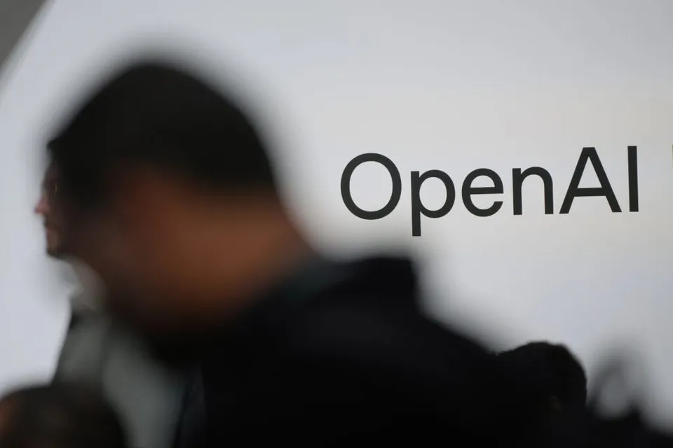 Un logo cu textul OpenAI este afișat pe un fundal alb lângă silueta neclară a unei persoane.