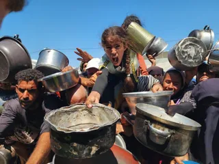 Un grup de persoane ține numeroase vase metalice de gătit sub un cer senin.