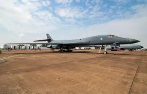 Un avion de vânătoare gri stă pe o pistă de beton sub un cer parțial înzăpezit cu nori albi.