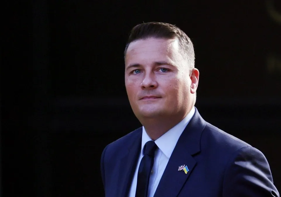 Un bărbat cu părul scurt, îmbrăcat în costum închis la culoare, cămașă albă și cravată neagră, poartă un pin cu steagul Ucrainei pe reverul sacoului.