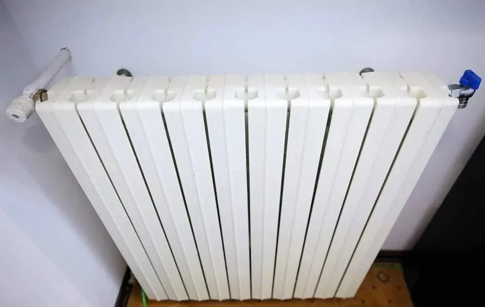 Un radiator alb montat pe un perete alb, cu robinetul de reglaj și supapa de aer vizibile la capete.