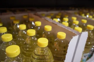Multe sticle de plastic cu capac galben, umplute cu un lichid galben, sunt așezate în cutii de carton într-un depozit întunecat.
