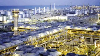 O vedere panoramică asupra unei instalații industriale complexe cu conducte, rezervoare de stocare și turnuri sub un cer de seară.