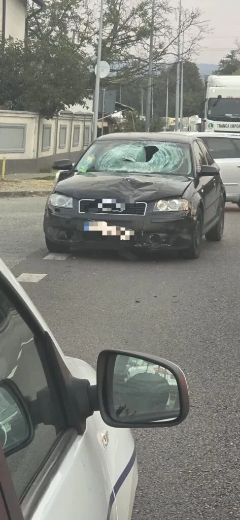 Un autoturism negru cu parbrizul spart stă pe un drum asfaltat lângă un vehicul alb.