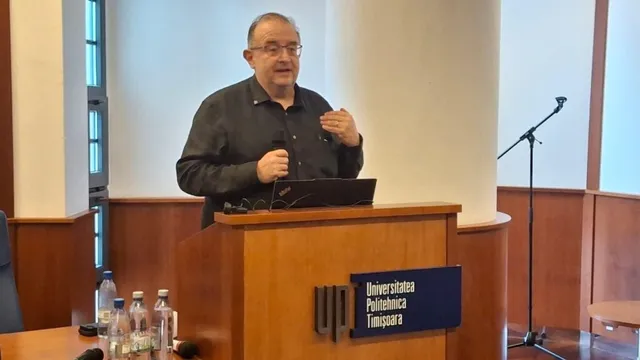 Un bărbat cu ochelari și costum negru vorbește dintr-un podium de lemn cu sigla Universității Politehnica Timișoara.