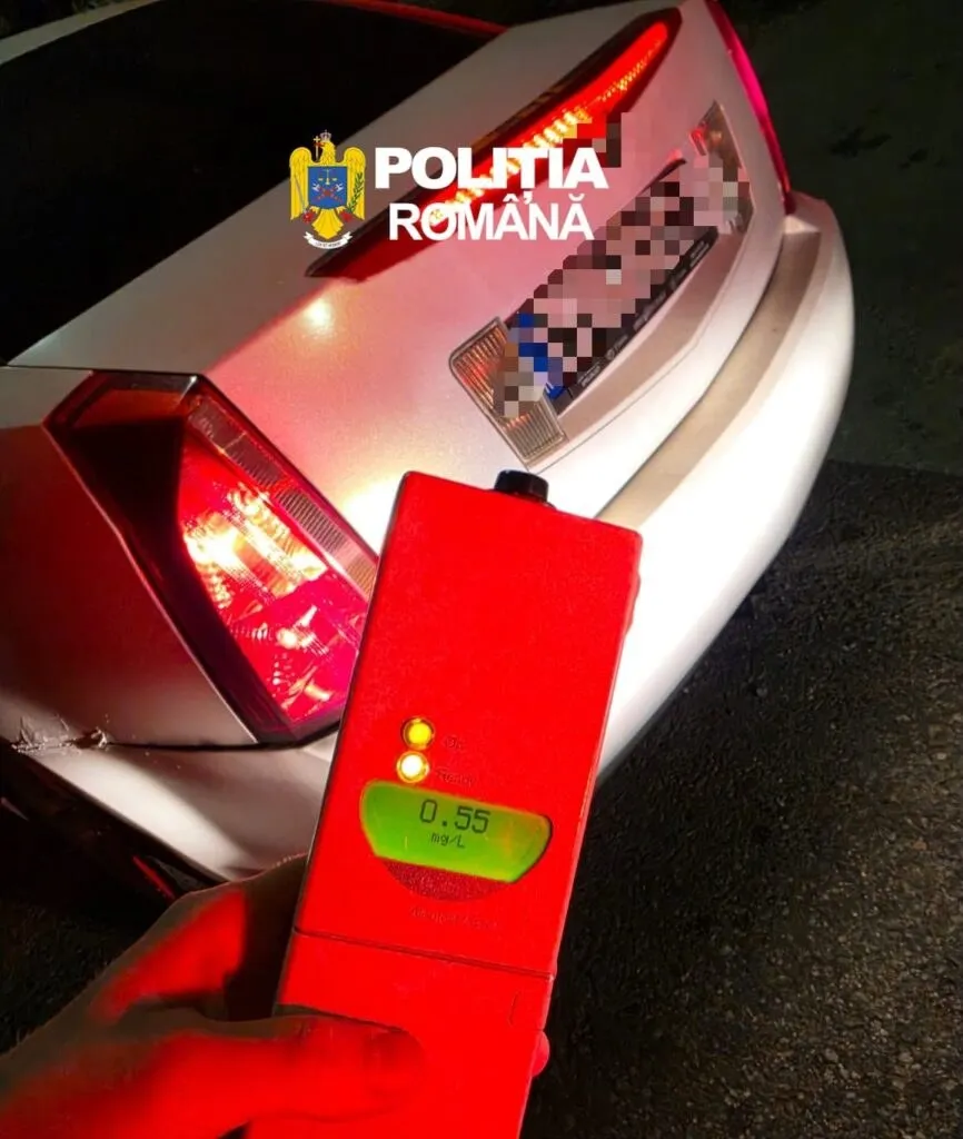 O mână ține un aparat de testare de culoare roșie cu un ecran digital afișând cifra 0,55 în fața unui autoturism alb.