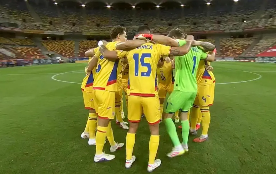 Un grup de fotbaliști în echipamente galbene și verzi stau îmbrățișați pe un teren de fotbal verde în interiorul unui stadion mare.