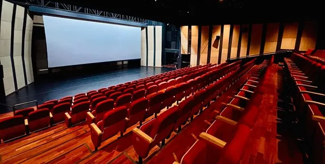 Interiorul unui cinematograf cu rânduri de scaune roșii orientate spre un ecran alb mare și o scenă întunecată.