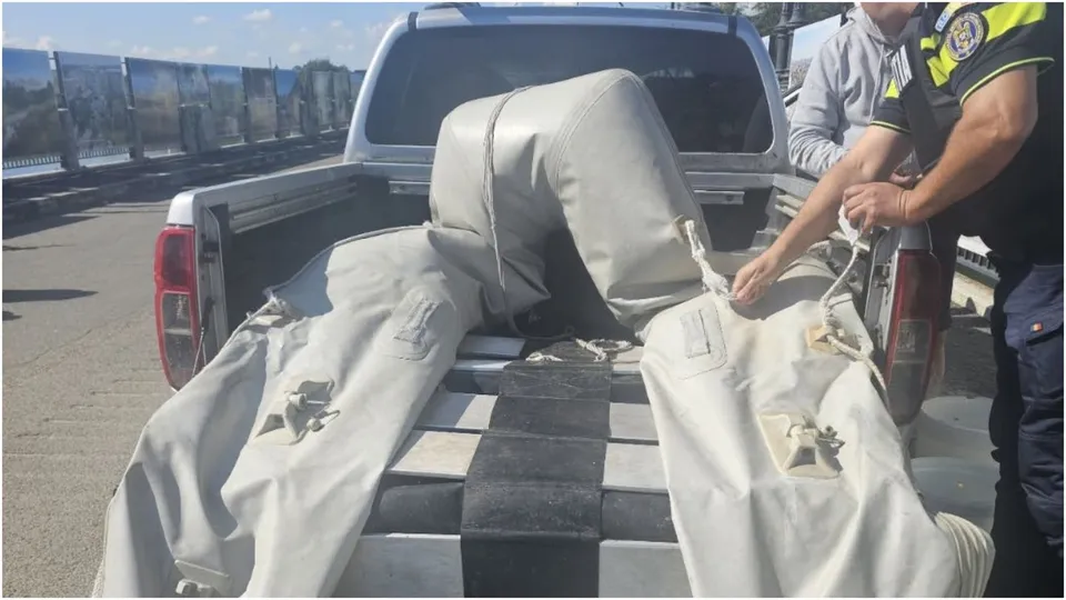 O persoană în uniformă manipulează o plasă de culoare deschisă aflată în partea din spate a unui pickup gri.