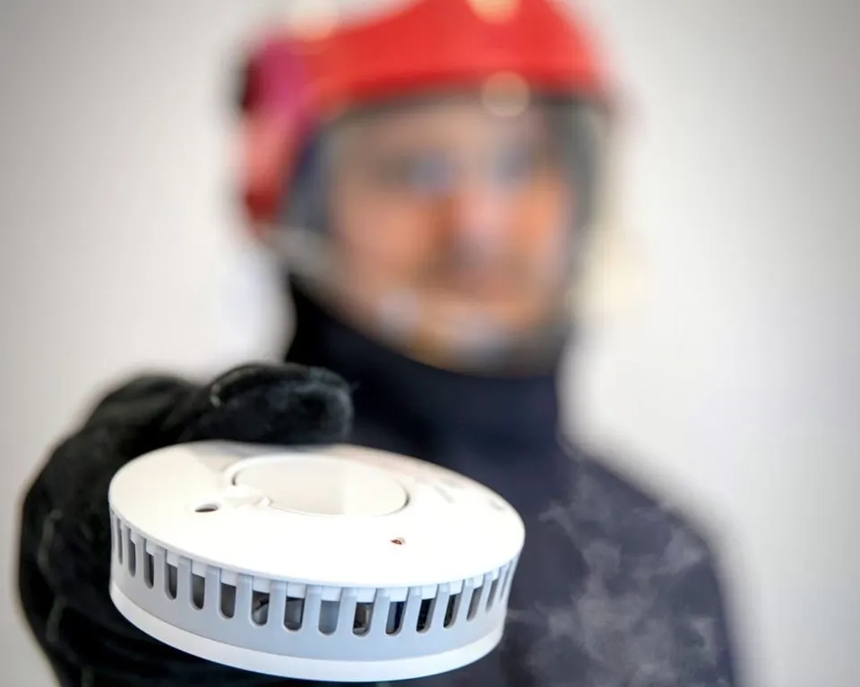 O persoană cu cască de protecție roșie ține un detector alb rotund în mână.