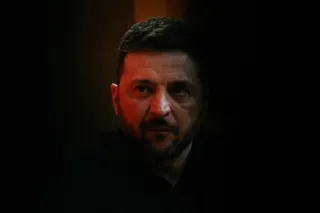 Un bărbat cu barbă și păr scurt, purtând o cămașă neagră, este surprins într-o lumină difuză pe un fundal întunecat.