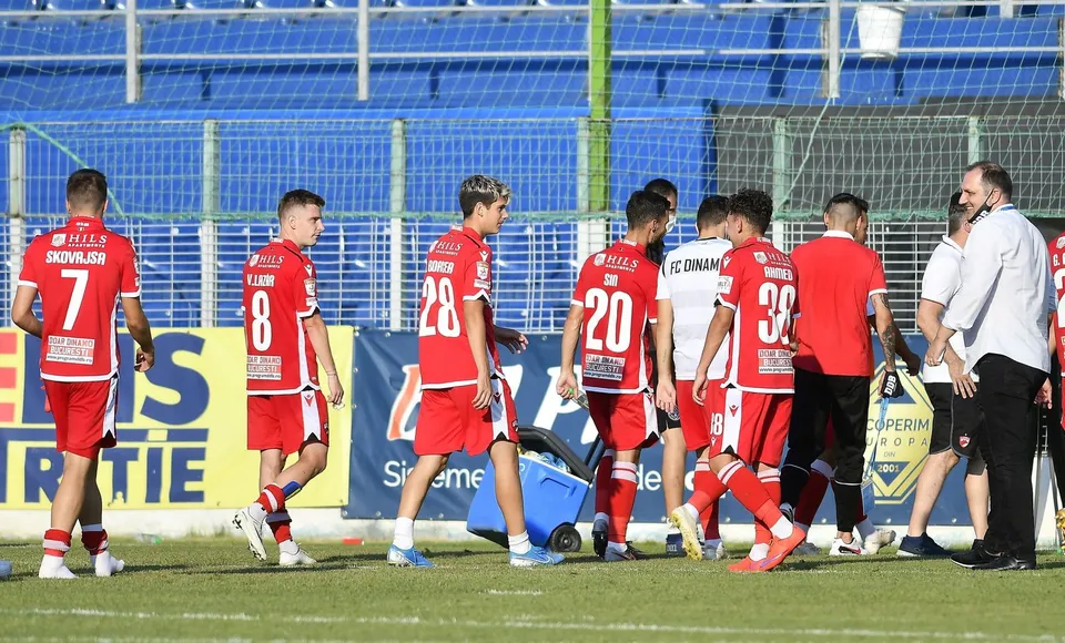 Cei mai mulți jucători de fotbal poartă echipamente roșii și merg pe un teren de fotbal verde în fața unor tribune albastre.
