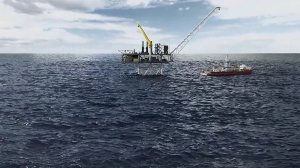 O platformă petrolieră cu o macara galbenă și o navă de lucru navighează pe o suprafață de apă sub un cer înnorat.