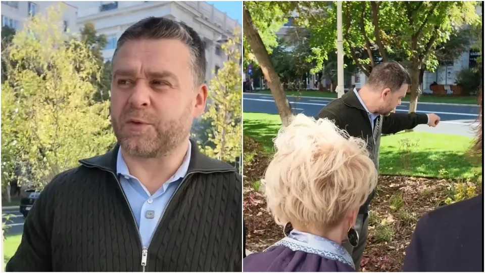 Un bărbat cu barbă și un pulover gri stă în fața unor copaci, în timp ce un alt bărbat arată spre o zonă cu iarbă verde.