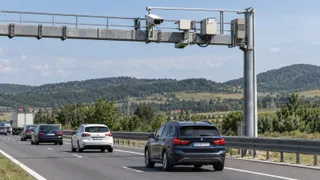 Mașini circulă pe o autostradă sub o structură metalică suspendată care conține echipamente electronice și camere de supraveghere.