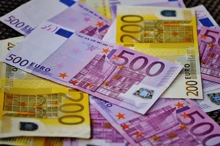 Bancnote euro roz și galbene, cu valori de 500 și 200, sunt suprapuse pe o suprafață întunecată.