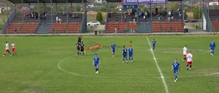 Jucători de fotbal în echipamente albastre și albe sunt pe un teren de fotbal verde, în fața unor tribune cu spectatori.