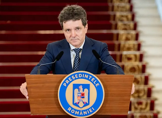 Un bărbat cu părul închis la culoare, purtând un costum albastru și cravată, stă în spatele unui podium de lemn cu un emblema circulară.