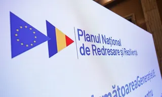 Un panou alb afișează steagul Uniunii Europene, steagul României și textul scris în albastru despre Planul Național de Redresare și Reziliență.