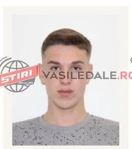 Un bărbat tânăr cu părul scurt și deschis la culoare poartă un tricou gri cu model punctat pe un fundal alb.