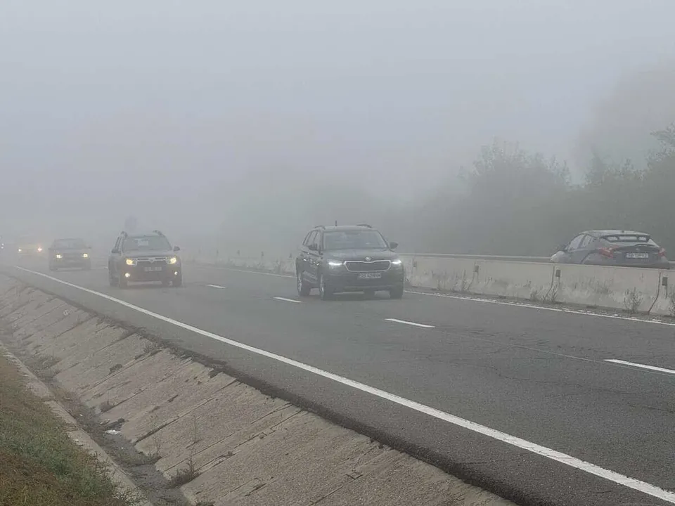 Mașini circulă pe un drum cu mai multe benzi într-un peisaj acoperit de o ceață densă care limitează vizibilitatea.