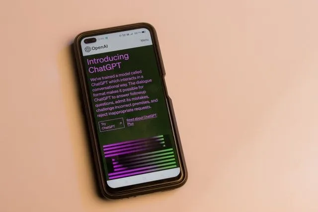 A phone on a pink surface displays an OpenAI/ChatGPT introduction screen with small unreadable text and colorful bars.