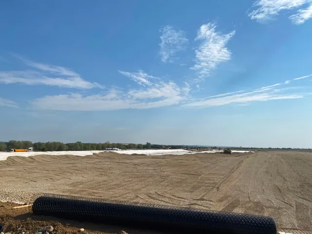 Un teren vast și plat cu pământ și materiale albe sub un cer albastru cu nori subțiri.