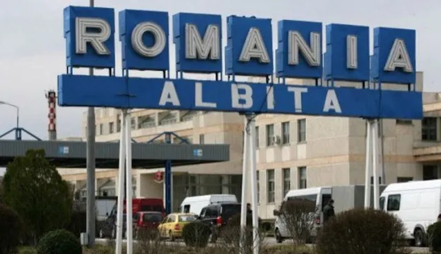 Un panou albastru cu litere mari albe indică intrarea în România prin punctul de trecere Albița, având clădiri și vehicule în fundal.