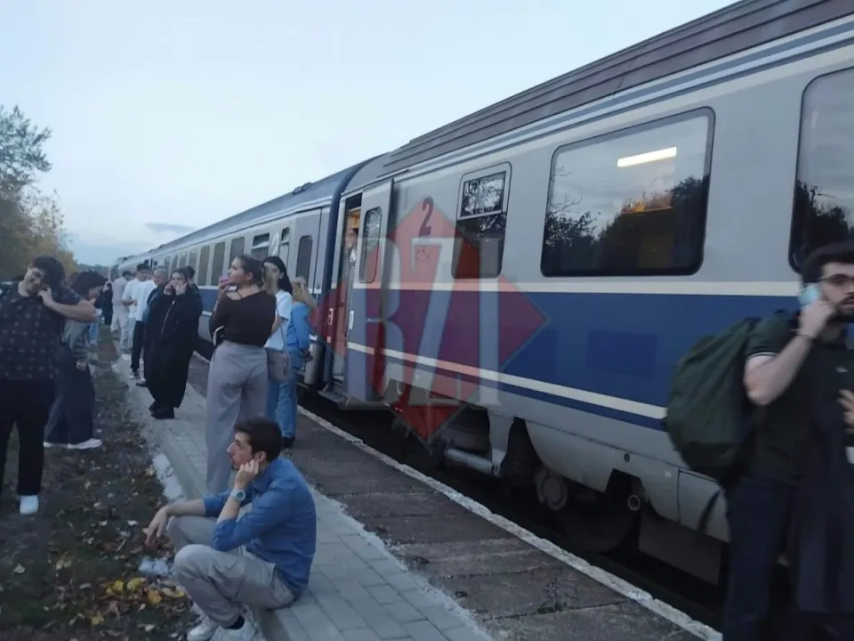 Oamenii stau pe marginea unui peron lângă un tren albastru și gri aflat pe șine.