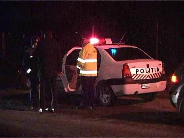 O mașină albă cu inscripția POLITIA este parcată pe un drum noaptea, lângă un vehicul cu portierele deschise și trei persoane în apropiere.