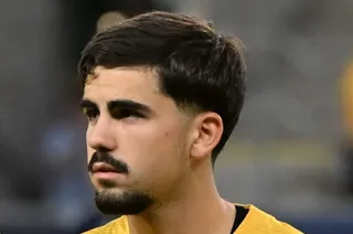 Un portret al unui tânăr bărbat cu păr negru scurt, mustăță și barbă scurtă, îmbrăcat într-o echipă sportivă galbenă.