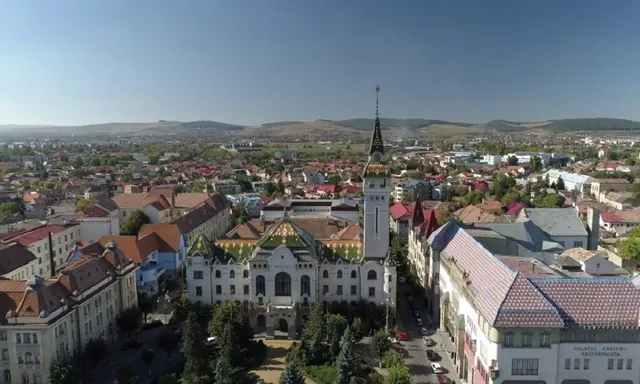 O vedere aeriană asupra unui oraș cu numeroase clădiri cu acoperișuri colorate și un turn înalt sub un cer senin.