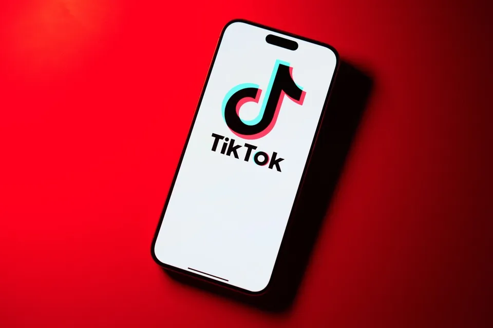 Un smartphone cu ecranul alb și logoul TikTok afișat este plasat pe un fundal roșu.