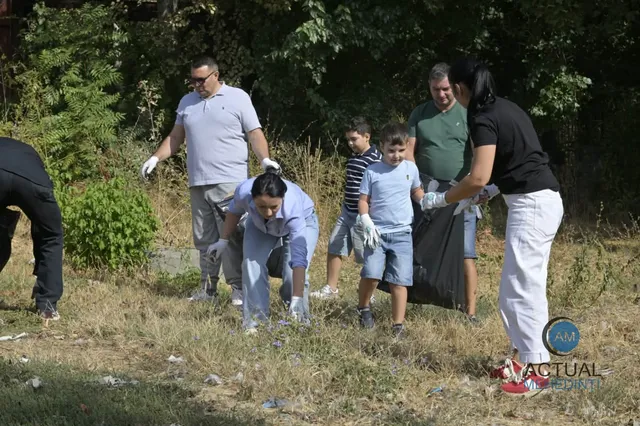 Un grup de persoane adună deșeuri dintr-o zonă cu iarbă uscată și vegetație, purtând mănuși de protecție și folosind saci negri.