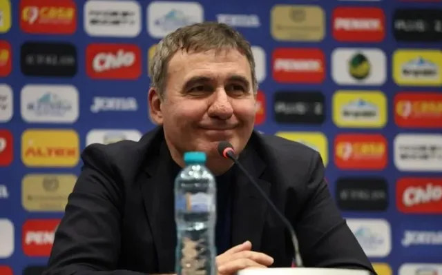 Un bărbat cu părul scurt și grijit, purtând un sacou închis la culoare, stă la o masă în fața unui fundal cu diverse logo-uri colorate.