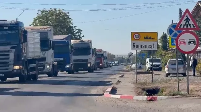 Mai multe camioane mari sunt parate pe un drum asfaltat lângă indicatoare rutiere și un semn de intrare în localitatea Romanești.