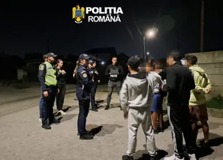 Mai mulți polițiști în uniformă stau pe o stradă noaptea, înconjurând un grup de civili.