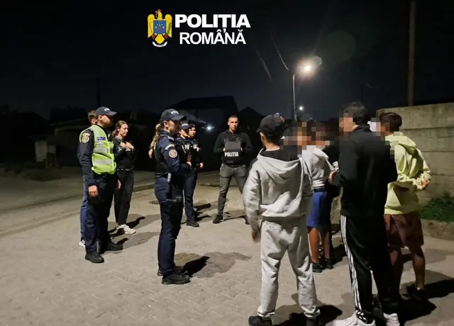 Mai mulți polițiști în uniformă stau pe o stradă noaptea, înconjurând un grup de civili.