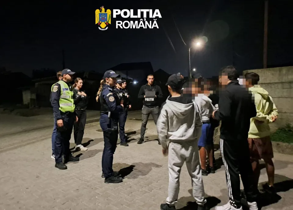 Mai mulți polițiști în uniformă stau pe o stradă noaptea, înconjurând un grup de civili.
